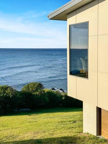 a window on the side of a building looking at the ocean at Ava - Luxe Oceanfront Beach House in Falmouth