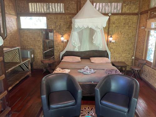 a bedroom with a bed and two chairs in it at Kupu Kupu Garden Guest House & Cafe in Bukit Lawang