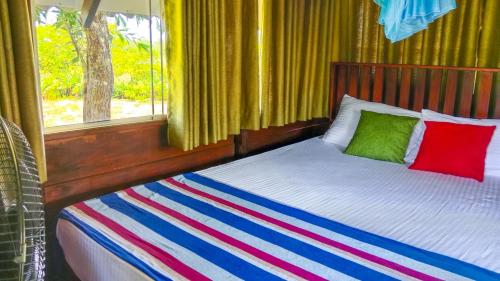 a bed with two colorful pillows and a window at Pride Rock Villa & Tree House in Sigiriya