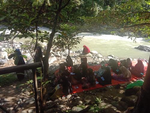 a group of people sitting on a blanket by the water at Sawah Resto Bungalow & Jungle Trekking in Bukit Lawang