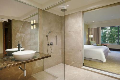 a bathroom with a shower and a sink and a bed at The Westin Pune Koregaon Park in Pune