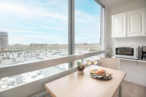 a kitchen with a table and a window with a view of a harbor at Face à Juno Beach - Appartement vue mer et port in Courseulles-sur-Mer