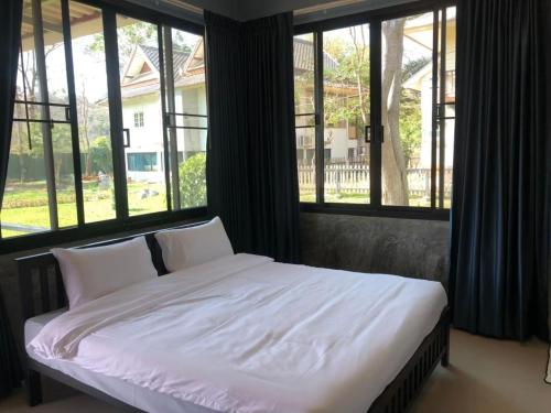 a bed with white sheets and pillows in a room with windows at Goldengold (Khaoyai) Resort & Spa in Mu Si