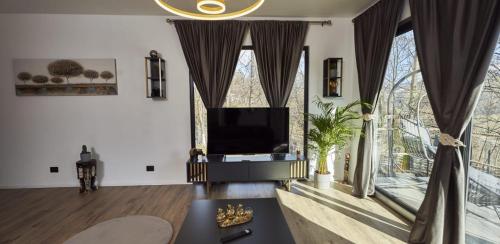a living room with a tv and large windows at Blissful Resort - Valea Doftanei in Teşila