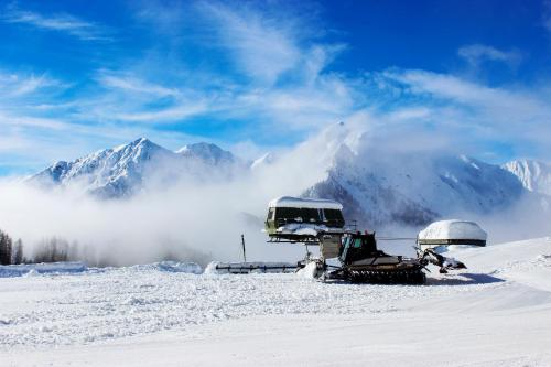 two snow vehicles parked in the snow with mountains in the background at Hotel Adler in Foppolo
