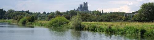 a river with tall grass and a castle in the background at A rural retreat with space and light in Birlingham