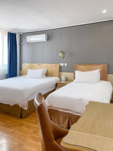 two beds in a hotel room with a chair at Qingdao Liuying Jieli Hotel - Qingdao Station Trestle Bridge Branch in Qingdao