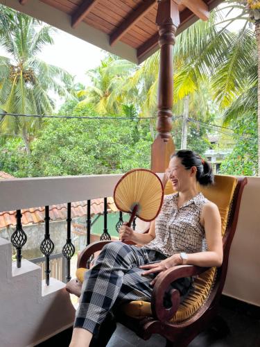 a woman sitting on a porch holding a fan at Villa Aroshina with cooking class in Galle