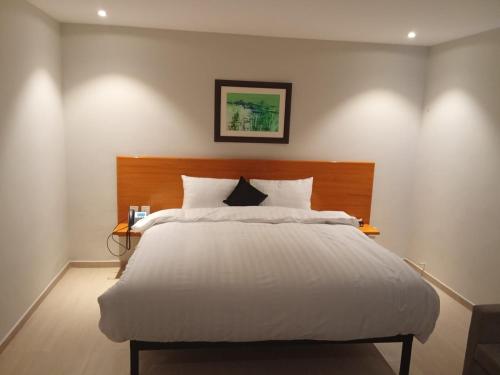 a bedroom with a white bed with a wooden headboard at The Avenue Hotel in Islamabad