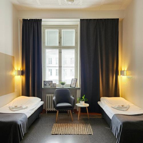 a room with two beds and a chair and a window at Hostel Bjorkenheim in Seinäjoki