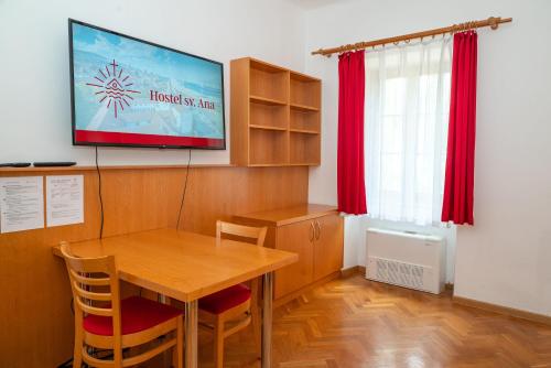 a dining room with a table and a tv on the wall at Hostel Sveta Ana in Koper
