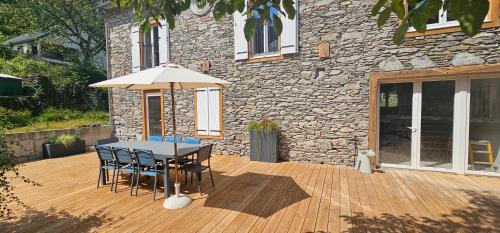 a table and chairs with an umbrella on a wooden deck at Gîte L'Ostau 4 étoiles Les Échappées Belles in Antignac