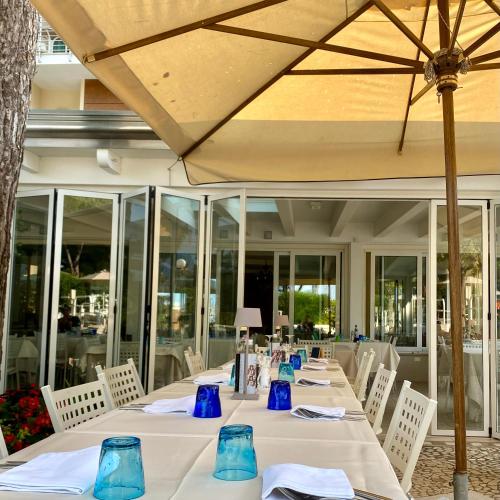a long table with white chairs and a umbrella at Hotel Franca in Milano Marittima