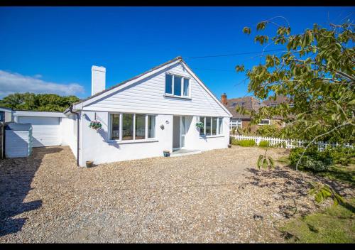 a white house with a gravel driveway at Bancroft - Camber Sands, East Sussex - Hot tub, parking for 6 cars, dog friendly in Camber