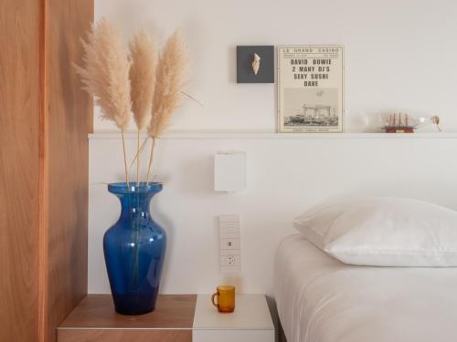 a blue vase sitting on a table next to a bed at Hôtel Vertime in Les Sables-dʼOlonne