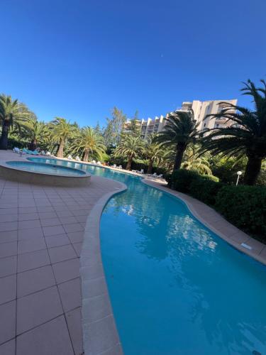- une piscine bordée de palmiers et de bâtiments dans l'établissement Appartement piscine tennis, à Mandelieu-la-Napoule