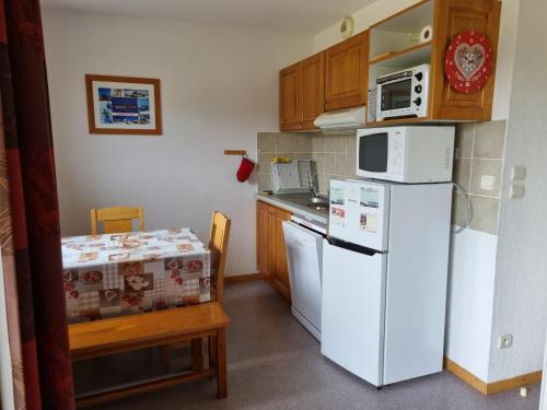 Elle comprend une petite cuisine équipée d'un réfrigérateur blanc et d'une table. dans l'établissement Grand 3 pièces cosy à SuperDévoluy (05) - Plein Sud, au pied des pistes, à Saint-Étienne-en-Dévoluy