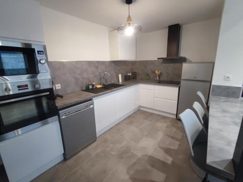 une cuisine avec des armoires blanches et des appareils en acier inoxydable dans l'établissement La petite maison de Laura située entre Caen Bayeux la mer, à Bretteville-lʼOrgueilleuse