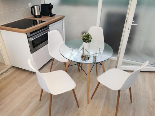 une petite cuisine avec une table en verre et quatre chaises blanches dans l'établissement 10 mins Center St Germain En Laye, à Mareil-Marly