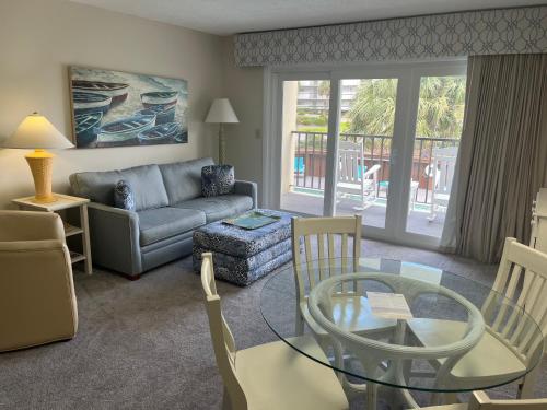 a living room with a couch and a glass table at Summer Sands - 106 by Sea Scape Properties in Wrightsville Beach