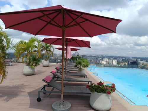 eine Reihe von Stühlen mit Sonnenschirmen neben einem Swimmingpool in der Unterkunft Skynest Residences by Lisa's Paradise D in Nairobi