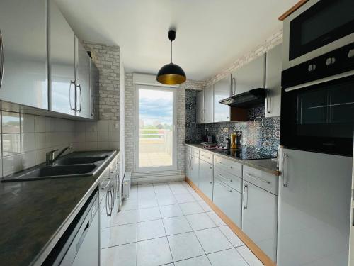 une cuisine avec des placards blancs et une grande fenêtre dans l'établissement Valenspot, à Valenciennes