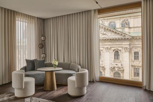 a living room with a couch and a table and a window at Koenigshof, a Luxury Collection Hotel, Munich in Munich