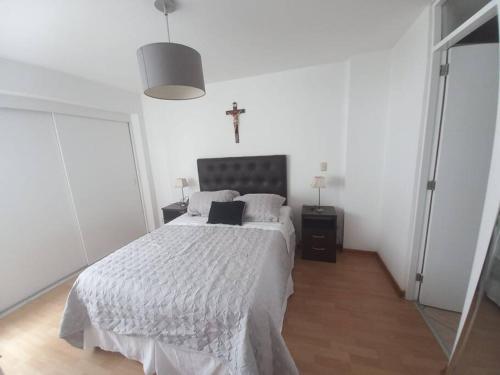 a white bedroom with a bed and a cross on the wall at Depa El Polo, Embajada USA, Surco in Lima