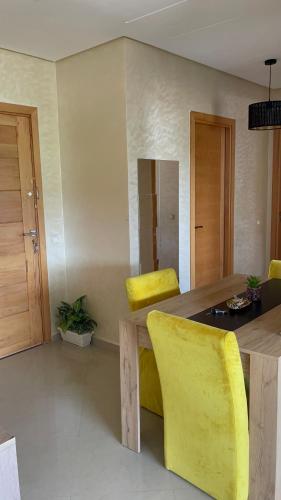 Appartement avec piscine à casa tamaris في دار بوعزة: غرفة طعام مع طاولة خشبية وكراسي صفراء