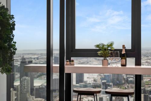 a table and two stools in front of a window at Gorgeous City Views 71st Floor 3BR Apartment with Pool and Gym in Melbourne