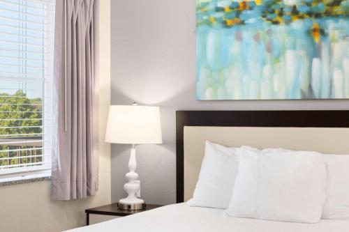a bedroom with a bed with a lamp and a window at WaterWalk Extended Stay by Wyndham Minneapolis - Plymouth in Plymouth