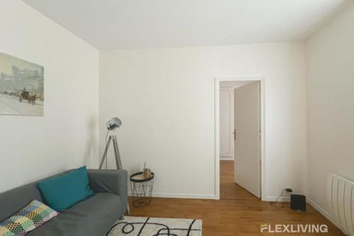 - un salon avec un canapé gris et un mur blanc dans l'établissement Flexliving - room - Villette, à Paris