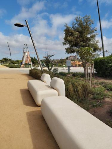a row of white benches sitting on a sidewalk at Primera línea de la playa en Casablanca in Aïn Harrouda