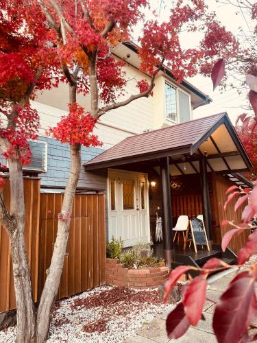 a house with a porch and a tree with red leaves at Hostel SAMURISE NORTH in Fujikawaguchiko