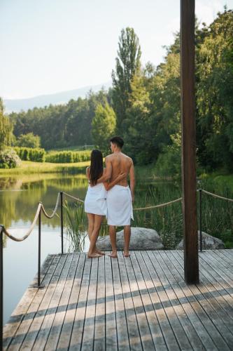 a man and woman standing on a dock near a lake at Hotel Seehof Nature Retreat in Naz-Sciaves