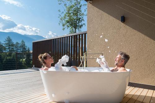 a man and woman in a bath tub on a deck at Hotel Seehof Nature Retreat in Naz-Sciaves