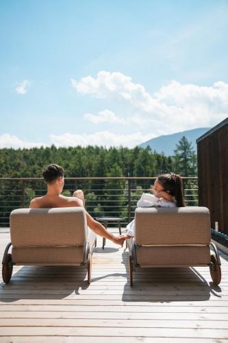 a man and a woman sitting in chairs on a deck at Hotel Seehof Nature Retreat in Naz-Sciaves