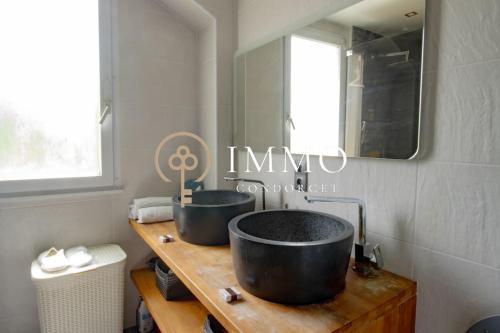 - une salle de bains avec deux lavabos noirs sur un comptoir en bois dans l'établissement Aux portes de Paris, à LʼHay-les-Roses