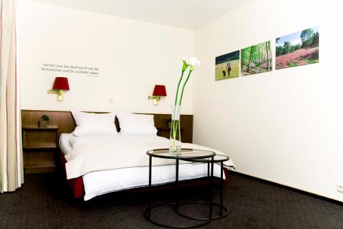 ein Schlafzimmer mit einem Bett und einem Tisch mit einer Blume darauf in der Unterkunft Hotel Restaurant Piärdestall Hövelhof in Hövelhof