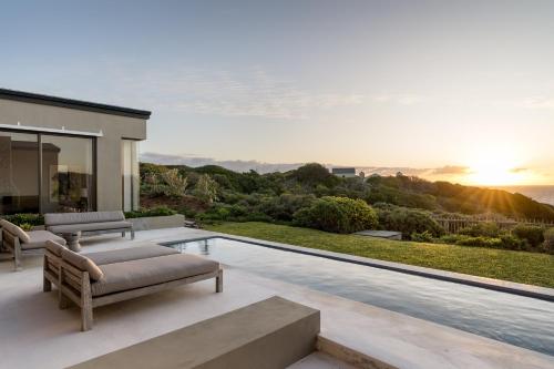 a villa with a swimming pool and a sunset at Romansbaai Collection in Gansbaai