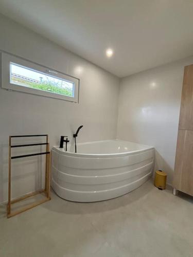 une grande salle de bains blanche avec baignoire et fenêtre. dans l'établissement Maison de campagne - L'escale bucolique, à Villefranche-de-Longchat