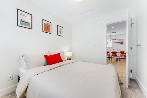 a white bedroom with a bed with a red pillow at Riley Park-Modern 4 Bedroom Home, Central location in Vancouver