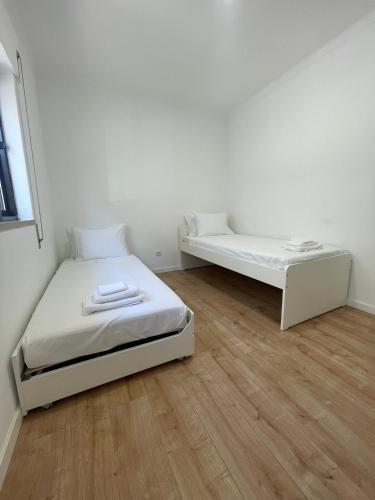 two beds in a white room with wooden floors at Sommer Apartment in Entroncamento
