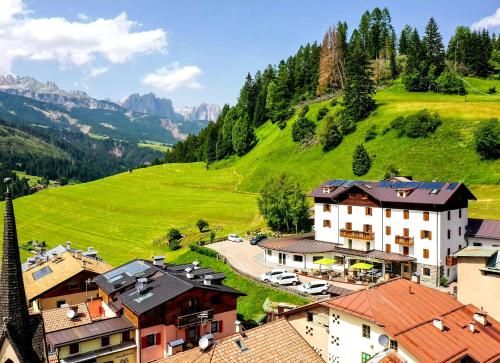 a village in the mountains with a green hill at Ciasa Alpina Relax Hotel in Moena