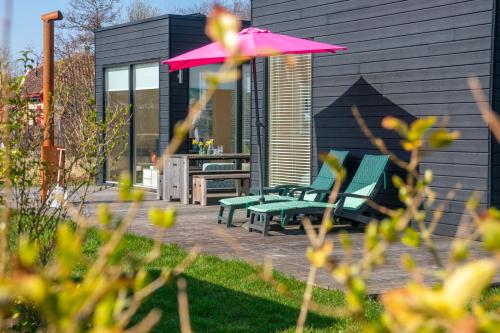 a patio with two green benches and a pink umbrella at Sterrenkijker - Ecohuisjes Terschelling in Midsland