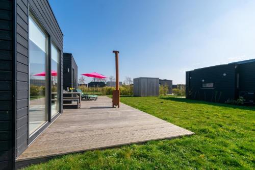 a wooden deck next to a building with a table and umbrella at Sterrenkijker - Ecohuisjes Terschelling in Midsland