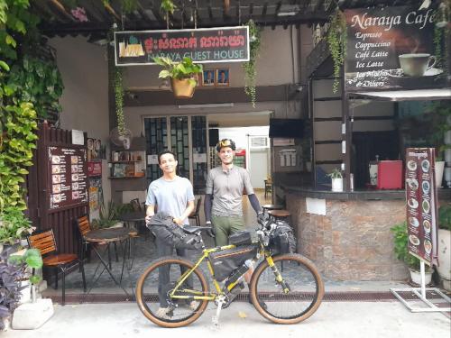 two men standing next to a bike in front of a shop at Naraya Guesthouse in Phnom Penh