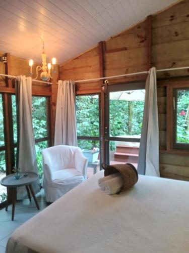 a bedroom with a bed and a chair and windows at LUGAR PERFEITO in Boicucanga