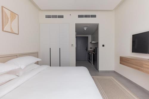 a white bedroom with a bed and a flat screen tv at Garden & Pool Access Studio in Sharjah
