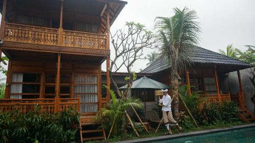 a man walking in front of a house with an umbrella at Harmony Wooden Villas in Ubud